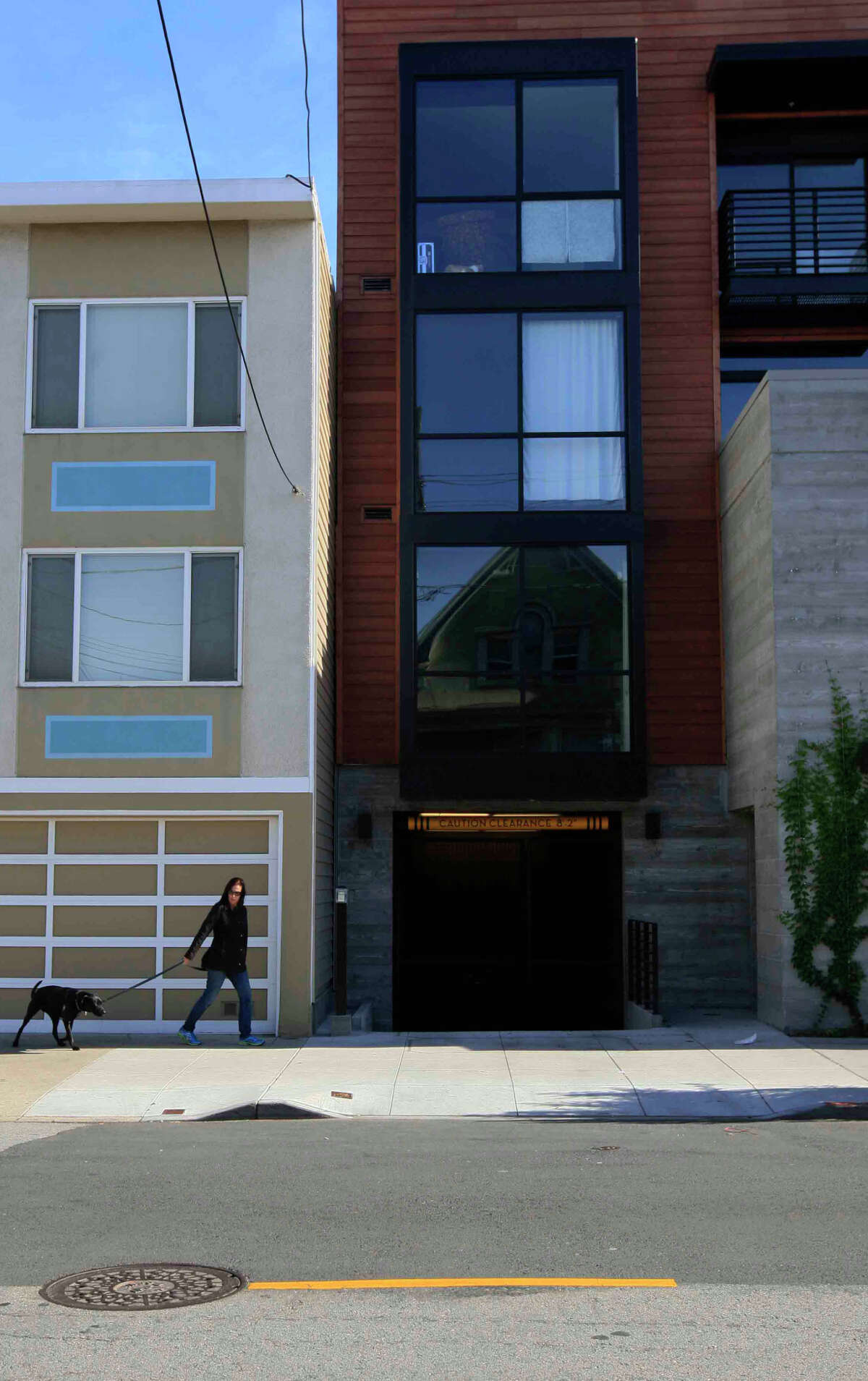 A woman and her dog walk past the residential building alongside the new mixed-use structure at 1266 9th Ave. in San Francisco’s Inner Sunset. In the center is the entrance to the 19-unit apartment building’s underground garage, which begins 9 feet in from the sidewalk.