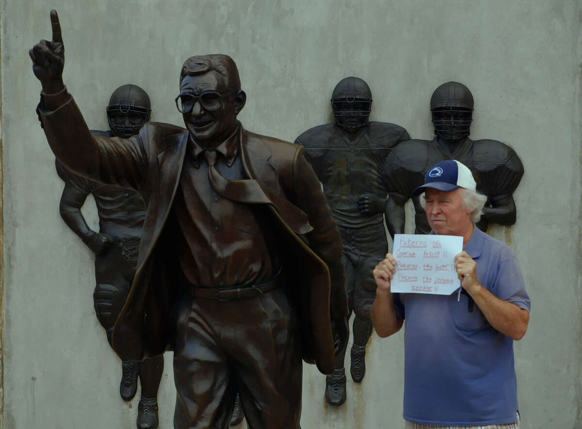 Bernie McCue protests next to a statue of Joe Paterno at Penn State.