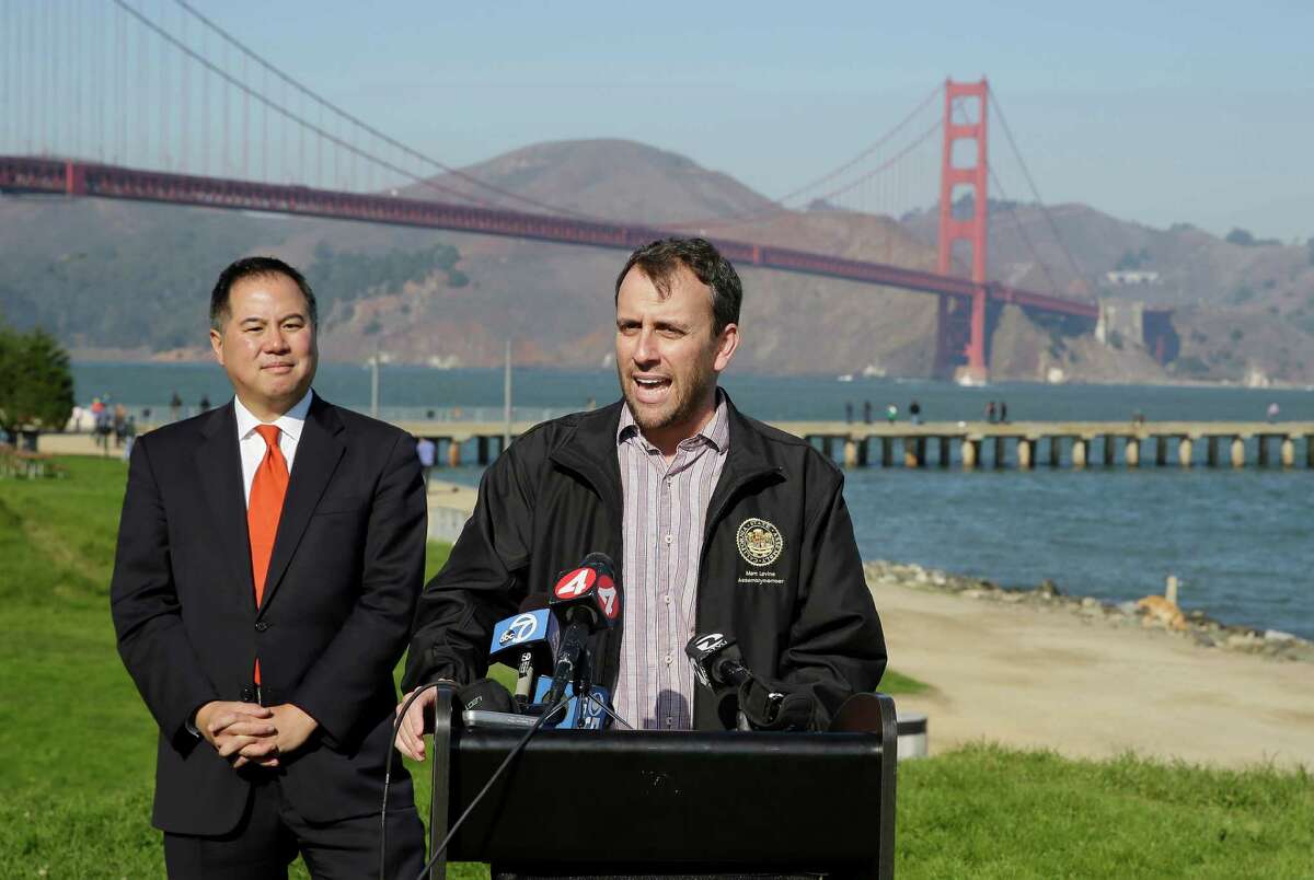 State assembly members Phil Ting, left, and Marc Levine, at podium, speak out against sidewalk tolls with the Golden Gate Bridge in the background during a press conference at Crissy Field Tuesday, Nov. 25, 2014, in San Francisco. The assembly members announced legislation to prevent the Golden Gate Bridge Highway and Transportation District from assessing a sidewalk toll on pedestrians and cyclists crossing the bridge. (AP Photo/Eric Risberg)