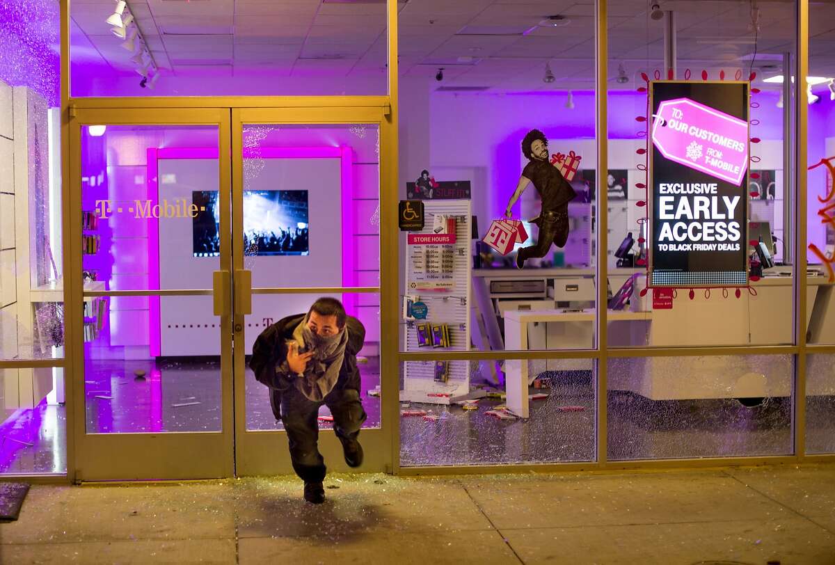 A man leaves a looted T-Mobile store in Oakland, Calif., on Tuesday, Nov. 25, 2014, a day after the announcement that a grand jury decided not to indict Ferguson police officer Darren Wilson in the fatal shooting of Michael Brown. Protesters briefly shut down two major freeways, vandalized police cars and looted businesses in downtown Oakland, smashing windows at cell phone stores, car dealerships, restaurants and convenience stores on a second night of protests. (AP Photo/Noah Berger)