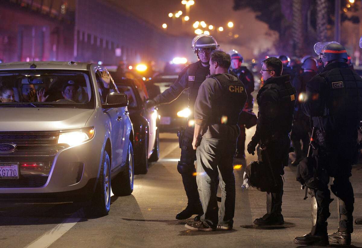 A driver and his passenger hold their hands up while they wait to be processed for citation and released on Wednesday, November 26, 2014, after CHP, Oakland Police and Alameda County Sheriff's officers raided a large sideshow event on Maritime Street in Oakland, Calif. Over 100 vehicles were trapped when law enforcement blocked both ends of the street, preventing almost everyone participating to be caught.