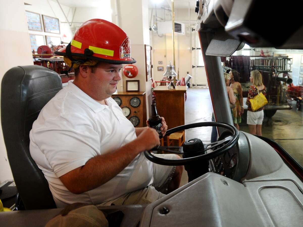 Zach Johnson dons a firefighter's hat as Jennifer Pate, not pictured, takes his photo at the Fire Museum of Texas during Thursday's Happy Hour event. The Beaumont Heritage Society hosted their second Happy Hour event, a bimonthly picnic held at historic sites around the Beaumont area, at the Fire Museum of Texas on Thursday evening. Executive Director Darlene Chodzinsai said the event is designed to draw new membership to the society, and that all proceeds from the events go toward preservation and the running of museums. Thursday night's event paired the society with Giglio's to bring the tastes of Abita to the museum. Photo taken Thursday 8/14/14 Jake Daniels/@JakeD_in_SETX