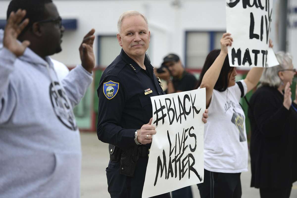In this photo taken Tuesday, Dec. 9, 2014, Richmond Chief of Police Chris Magnus stands with demonstrators along Macdonald Ave. to protest the Michael Brown and Eric Garner deaths during a peaceful demonstration in Richmond, Calif. The Northern California police chief noted for his community policing efforts raised a few eyebrows when he joined a peaceful protest, holding a sign with the popular Twitter hashtag of "blacklivesmatter." Magnus said he attended to show the department's commitment to peaceful protest and that minority lives matter. (AP Photo/Bay Area News Group, Kristopher Skinner)