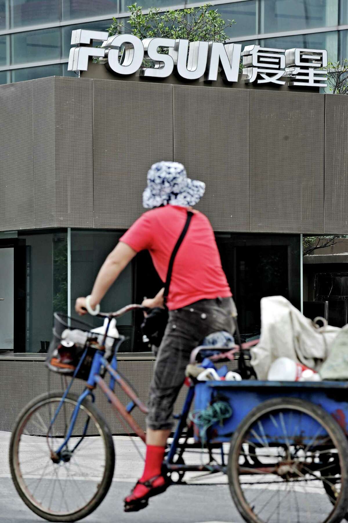 A woman rides a tricycle past the logo of Fosun Group, in front of the company's headquarters building in Shanghai on June 15, 2010. Chinese investment company Fosun bought a seven-percent stake in French leisure group Club Med, which is looking to tap the growing Chinese tourism market whose revenue last year totalled one trillion yuan (146 billion USD, 121 billion Euro). AFP PHOTO/PHILIPPE LOPEZ (Photo credit should read PHILIPPE LOPEZ/AFP/Getty Images)
