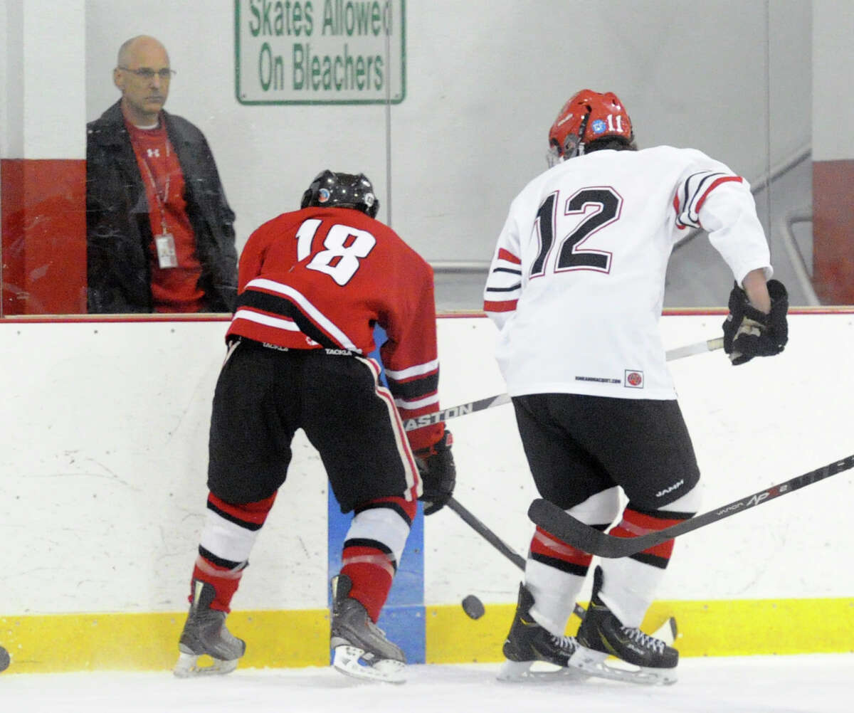 At left, Casey Begoon (#18) of New Canaan goes for a loose puck along with Brian Silard (#12) of Greenwich during the boys hockey game between Greenwich High School and New Canaan High School at Hamill Rink in Greenwich, Conn., Tuesday night, Dec. 23, 2014. Greenwich won 3-2 in overtime on a Silard goal.