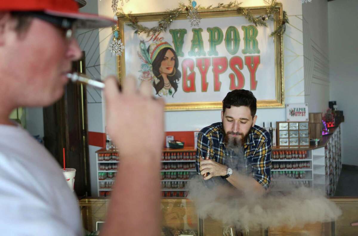 Adam Farrar, Assistant Manager at Vapor Gypsy, answers questions for customer Josh Eason, 19, at Vapor Gypsy. Farrar cards minors wanting to purchase e-cigarettes on Monday, Dec. 22, 2014, in Houston. Texas legislators will consider making it illegal for minors to buy electronic cigarettes, the "safer" alternatives to smoking that's become popular among youth.