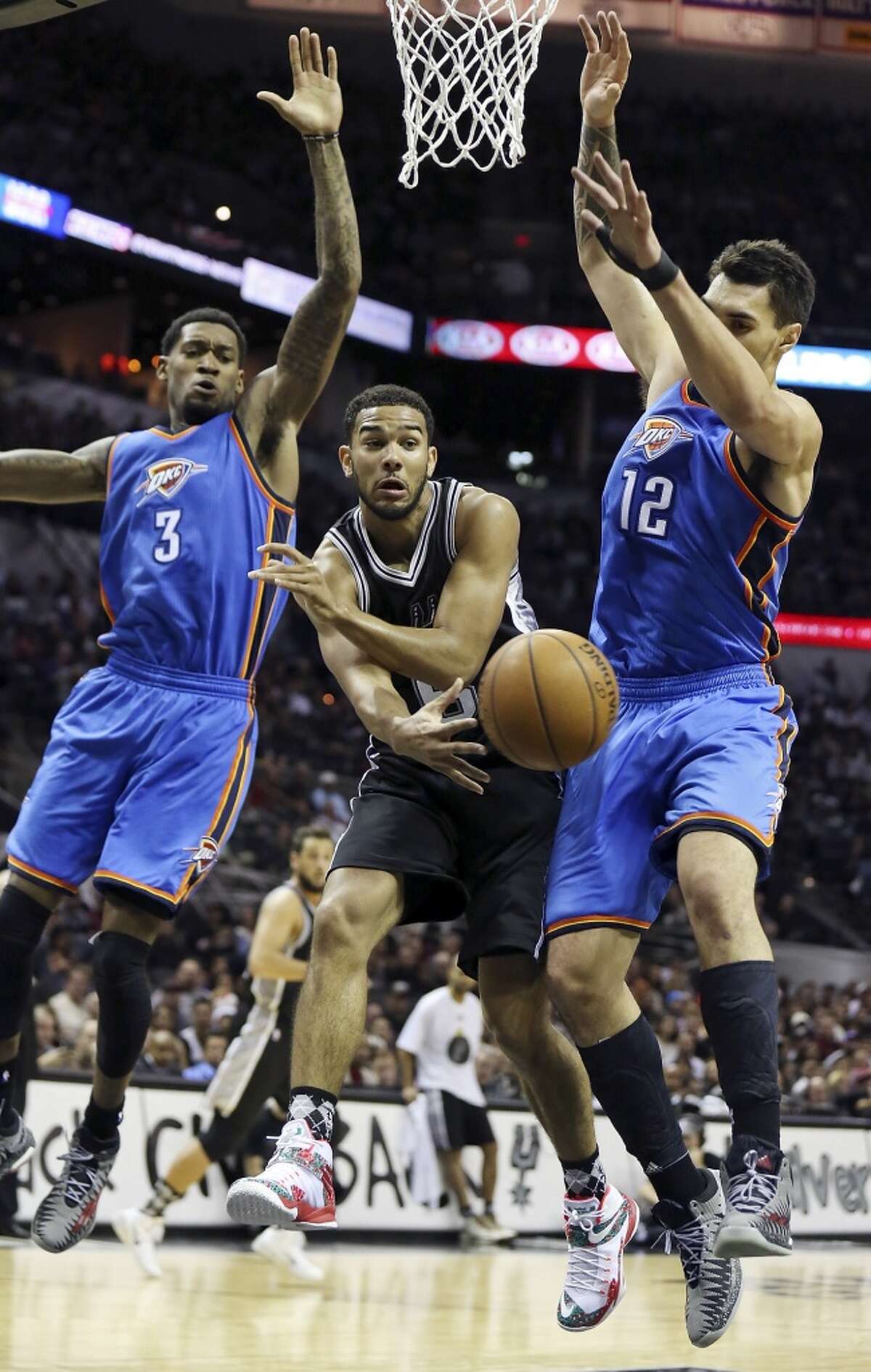 San Antonio Spurs' Cory Joseph passes between Oklahoma City Thunder's Perry Jones (left) and Steven Adams during first half action Thursday Dec. 25, 2014 at the AT&T Center.