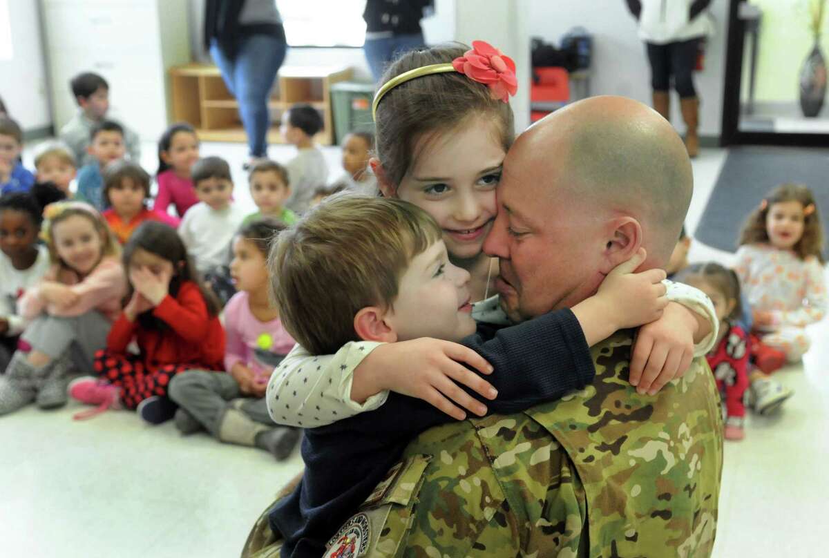 Christian, 3, and Jordyn Geanuracos, 6, hug their father after he surprised them with a visit to their school, New England Country Day School in Danbury, Conn. Friday, March 7, 2014. Thomas Geanuracos, 41, a Danbury police officer and Air National Guardsman stationed in Iraq for the past six months.