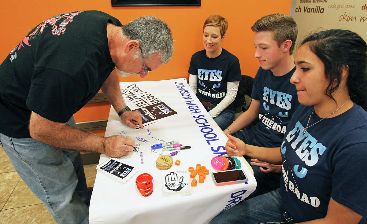 Jerry Alexander signs the pledge not to drive and text as Johnson High School students (right) Brittany Muller and Tyler Otten team up with parent advisor Melinda Cox at Duncan Donuts on TPC Parkway to inform customers of the upcoming new laws concerning texting and driving and also to warn against the dangers of using hand held devices while driving on December 27, 2014.