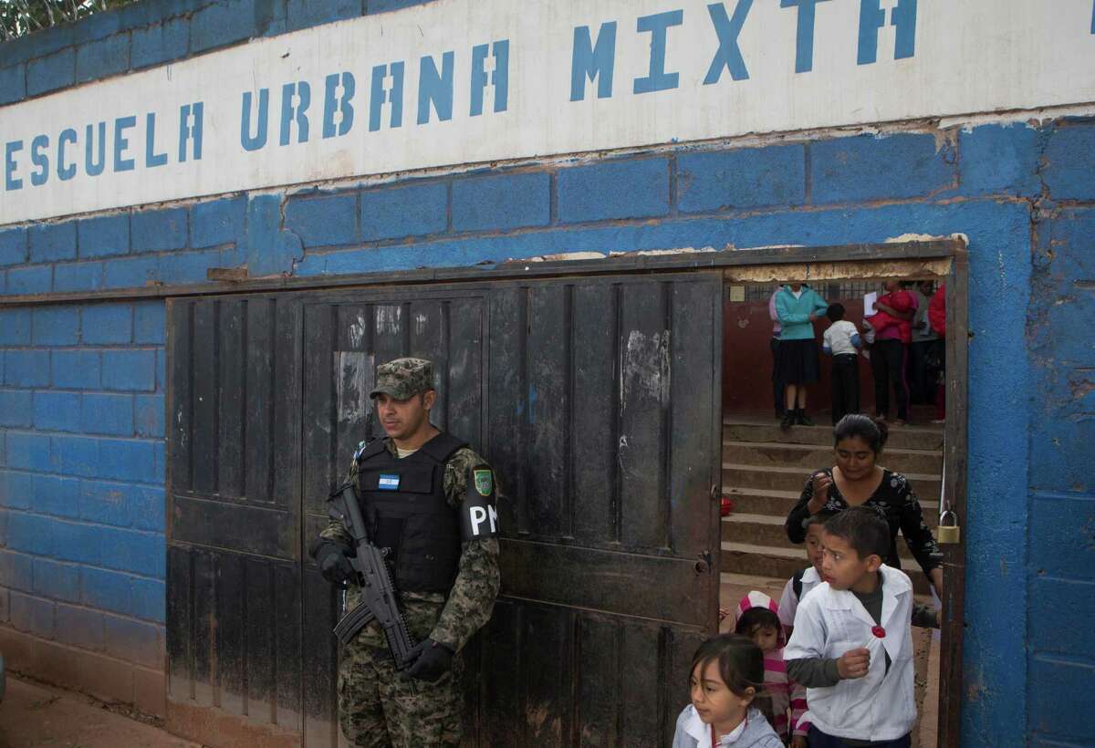 In this photo Nov. 28, 2014 photo, a member of Hondura's Military Police, stands guard at the entrance of a school, during the last day of class, in the Canaan neighborhood of Tegucigalpa, Honduras. Street gangs control most schools in Tegucigalpa, where a lot of the students are gangsters, along with their parents. (AP Photo/Esteban Felix)