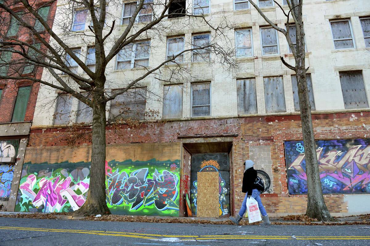 A woman makes her way past a block of closed buildings which are part of downtown north in Bridgeport, Conn. on Thursday Jan. 8, 2015. Mayor Bill Finch announced a city plan to develop these buildings and make them into apartments and businesses.