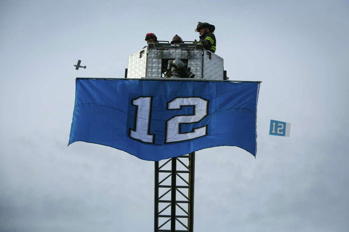 An airplane towing a flag flies behind a flag unfurled from a Renton Fire Department ladder truck during a Seattle Seahawks fan rally at Renton City Hall on Friday, January 9, 2015. Hundreds of Seahawks fans came to the rally to show support for the Hawks before their playoff matchup with the Carolina Panthers.
