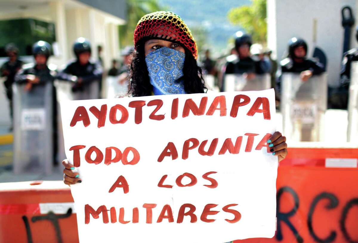 A woman holds a banner reading “Ayotzinapa, everything points to the military” during a protest demanding justice.