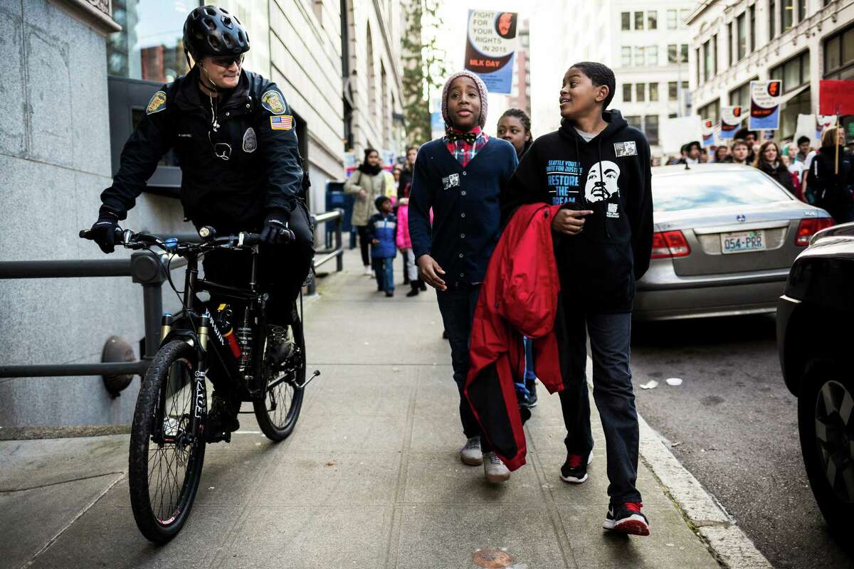Kameron Port, right, joined by Khaim Vassar, center, take to the sidewalk to have a friendly chat with Officer R. Martinez, left, during the 33rd annual "Rise Up! Restore the Dream!" celebration for Martin Luther King, Jr., on Monday, Jan. 19, 2015, in Seattle, Washington. The mass of walked from Garfield High School to downtown Seattle.
