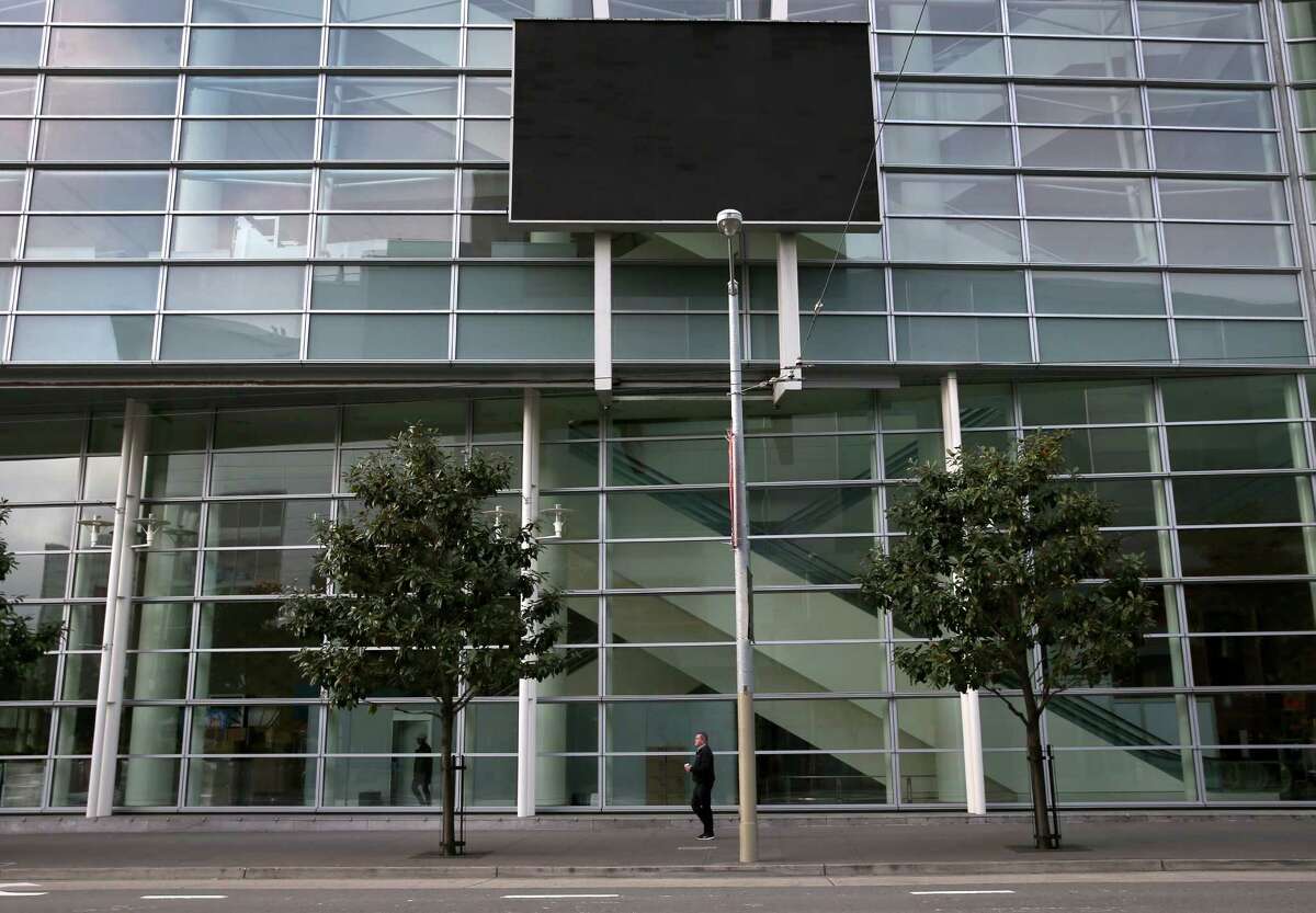 A man walks beneath a dark video screen installed on the side of Moscone West on Fourth Street in San Francisco, Calif. on Tuesday, Jan. 20, 2015. The screen has never really functioned since its installation in 2003.