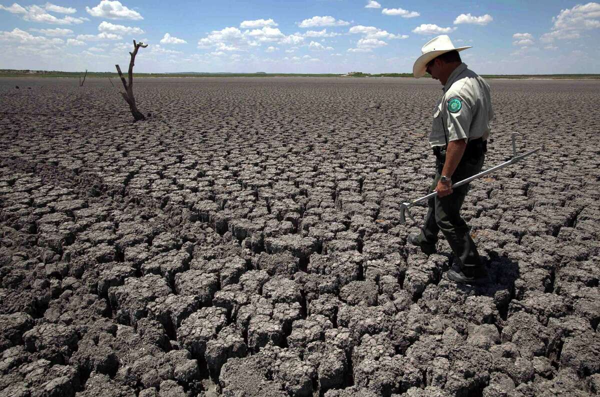In this Aug. 3, 2011, file photo, Texas State Park police officer Thomas Bigham walks across the cracked lake bed of O.C. Fisher Lake in San Angelo, Texas. Scientists believe that warming and the weather swings it brings are already affecting people's lives.