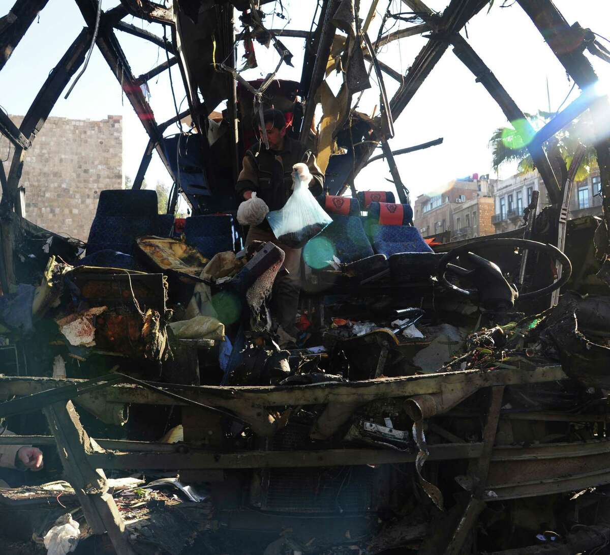 In this photo released by the Syrian official news agency SANA, a man, at centre, collects items from inside a destroyed Lebanese tour bus after a bomb attack, in Damascus, Syria, Sunday, Feb. 1, 2015. A bomb placed on the bus ferrying Lebanese pilgrims around Shiite holy sites in Damascus exploded Sunday, killing at least seven people, according to Syrian activists and Lebanese media, underscoring the sectarian nature of Syria's four-year war.