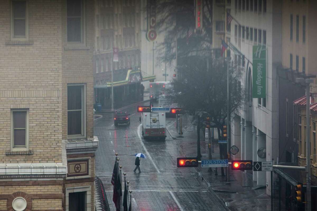 A person walks in the rain across St. Mary's St. in downtown San Antonio on Tuesday, February 3, 2015.