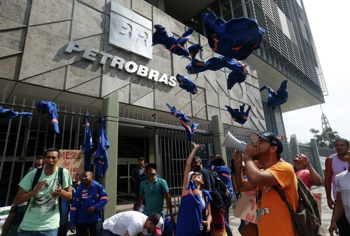 Workers whose company is contracted by Brazil's government-run oil company Petrobras throw their work uniforms at Petrobras headquarters to protest corruption and that they haven't been paid in Rio de Janeiro, Brazil, Wednesday, Feb. 4, 2015. Petrobras said Wednesday the company's chief executive officer and five other top figures stepped down amid a long-running and massive kickback scandal at the firm. (AP Photo/Silvia Izquierdo)