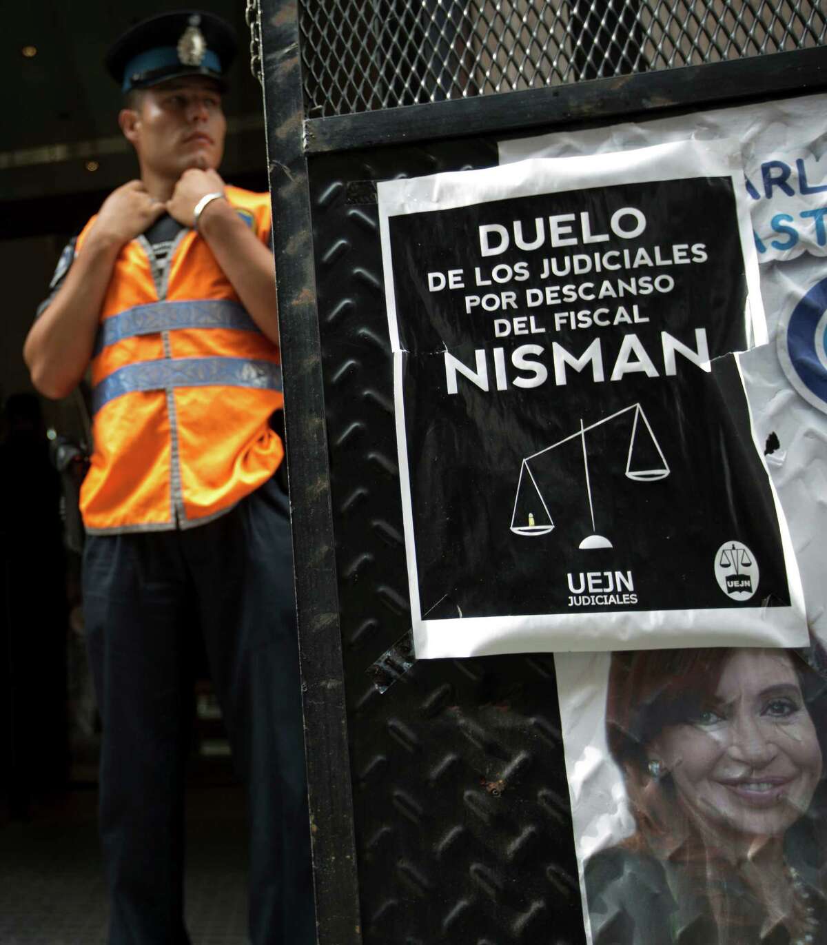 A police officer stands guard in front of he prosecutor's office that leads the investigation of prosecutor Alberto Nisman's death, in Buenos Aires, Argentina, Thursday, Feb. 5, 2015. Posted on the gate is a portrait of Argentina's President Cristina Fernandez along with another poster that reads in Spanish "Mourning of judicial workers due to the death of prosecutor Nisman." Investigators examining the death of Nisman who accused President Fernandez of agreeing to shield the alleged masterminds of a 1994 terror bombing said Tuesday they found a draft document he wrote requesting her arrest. (AP Photo/Rodrigo Abd)