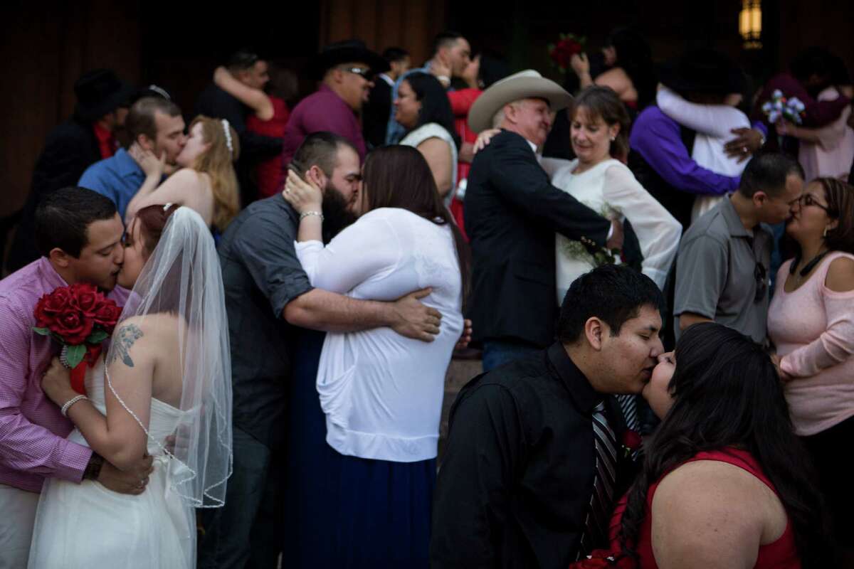 Alyssa and Greg Kogutz, left, kiss while Pablo Gonzales kisses Leah Gonzales, lower right, during one of the free mass wedding ceremonies held annually on the steps of the Bexar County Courthouse on Valentine's Day, Saturday, February 14, 2014. Over 30 couples married during this ceremony, which was held at noon.