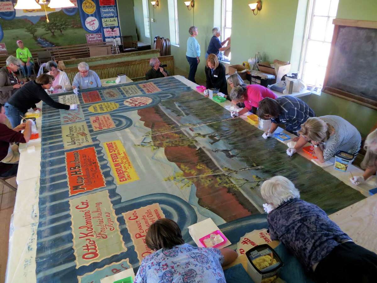 Volunteers help clean the antique curtain that once hung in the second-floor stage area of the Willow City School in Gillespie County. The curtain is believed to have been created around 1930.