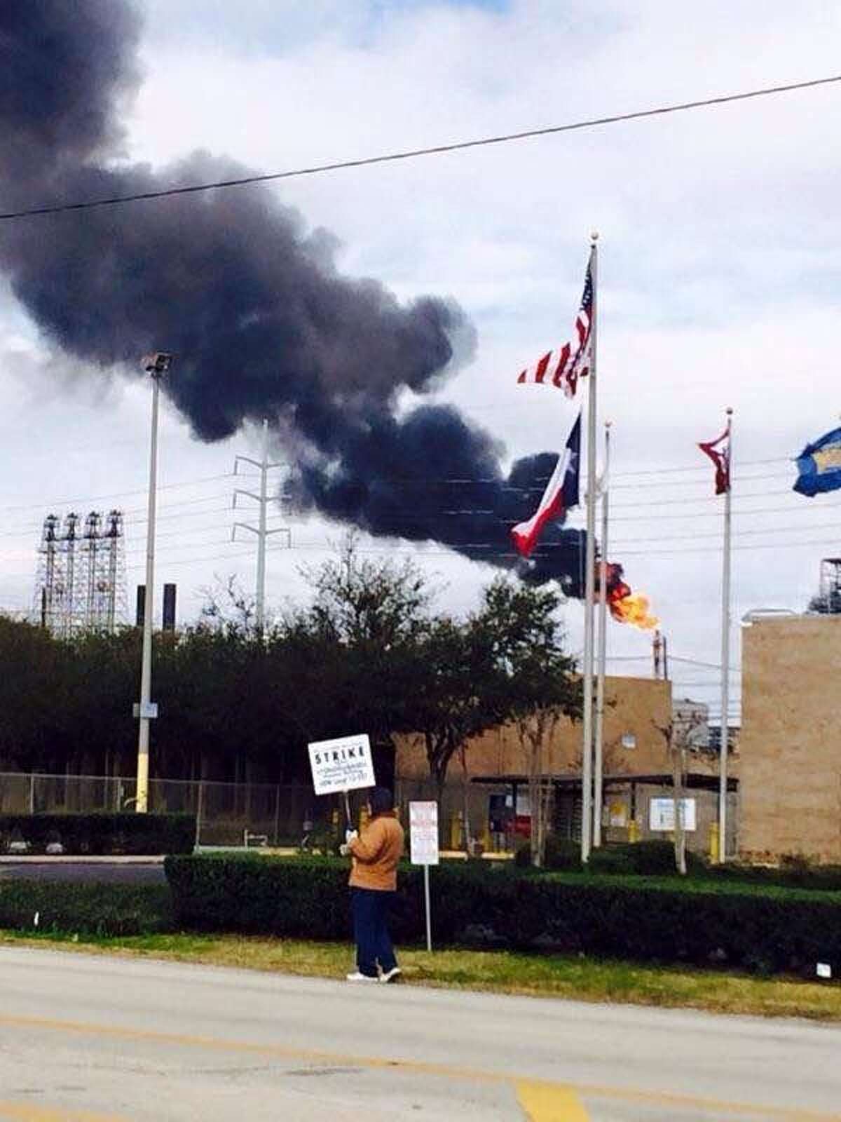 In a photo provided by striking steelworker Juan Almanza, black smoke from a flaring stack rises behind a picketer at LyondellBasell's Houston refinery on Feb. 17, 2015. Strikers say the flare illustrates safety concerns that are among issues in the labor negotiations, but LyondellBasell spokesman George Smalley characterized the incident as a "brief upset" resulting from a tripped compressor at a refining facility called a delayed coker unit. He said the situation did not become an emergency, safety systems functioned as designed and the flare burned off associated gas until the compressor resumed operations about 30 minutes later.