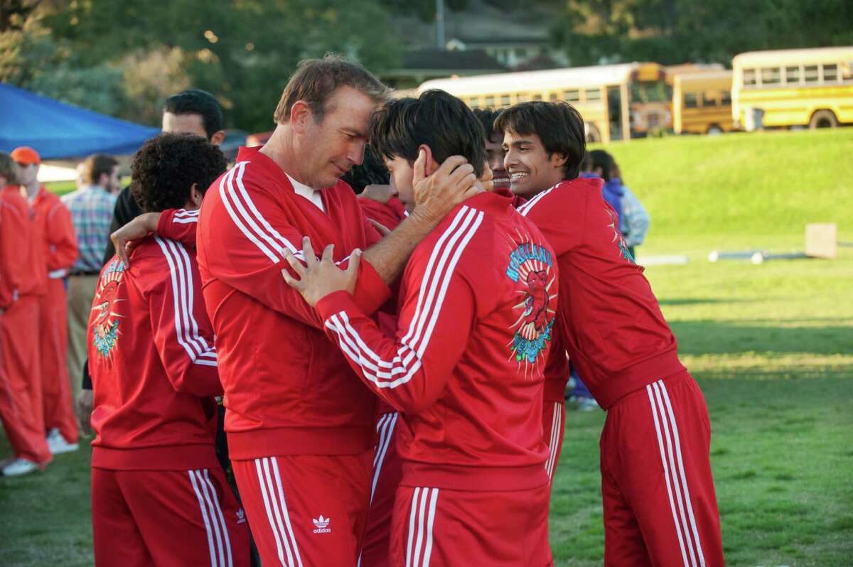 Kevin Costner (left foreground) as the coach of impoverished students embraces Carlos Pratts in “McFarland, USA,” a movie that makes us care despite its unsurprising theme.