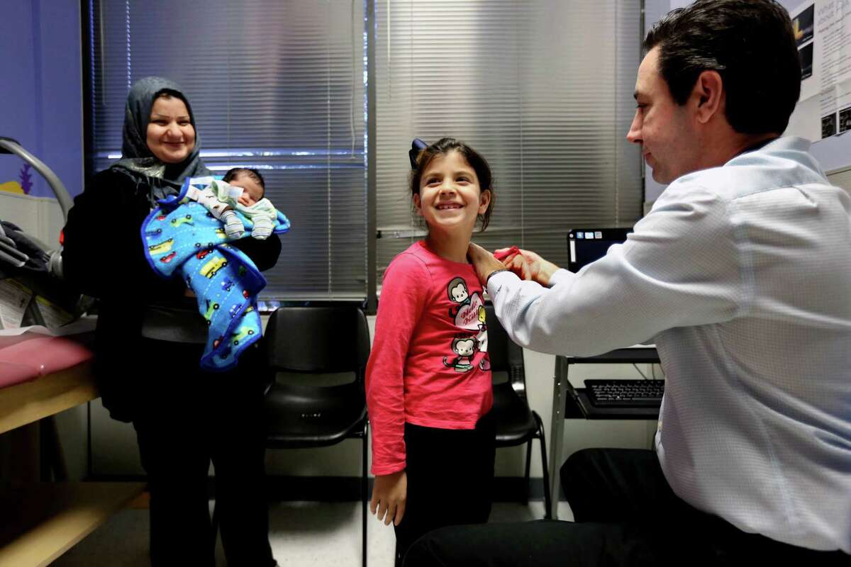 Dr. Peter Palmieri examines Fatimah Hussein, 7, while her mother, Hiba Kadham, holds newborn brother Mosa Hussein ﻿at HOPE Clinic, a community health center established by the Asian American Health Coalition.﻿