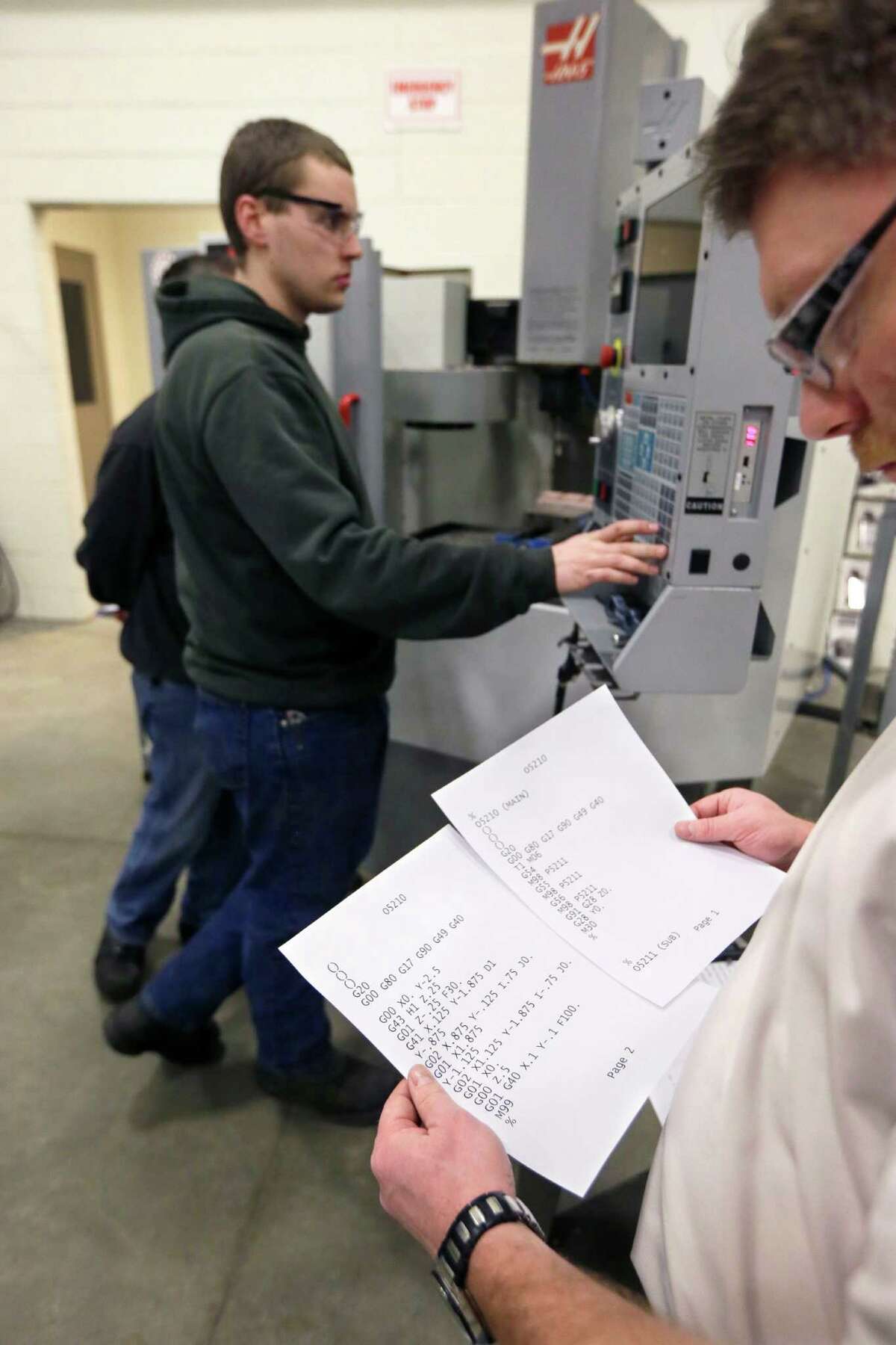In a photo from Wednesday, Feb. 11, 2015 in Lansing, Mich., Lansing Community College adjunct instructor Marty Kroell looks over computer code as Travis Reglin works on a computer numerical control mill in the advance precision machining class. Gov. Rick Snyder wants to re-establish vocational and technical schooling as an âequally honorable, equally important and equally well-compensatedâ career track. To that end, his new budget proposes a $36 million, or 75 percent, increase in spending on trades training, technical education and career planning. (AP Photo/Carlos Osorio)