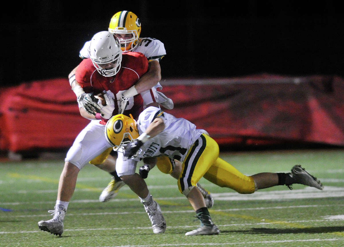 Greenwich's Scooter Harrington is brought down by Trinity Catholic's Nick Melia, right, and Thomas Costigan, background, during their football game at Greenwich High School in Greenwich, Conn., on Thursday, Oct. 2, 2014. Greenwich won, 28-13.