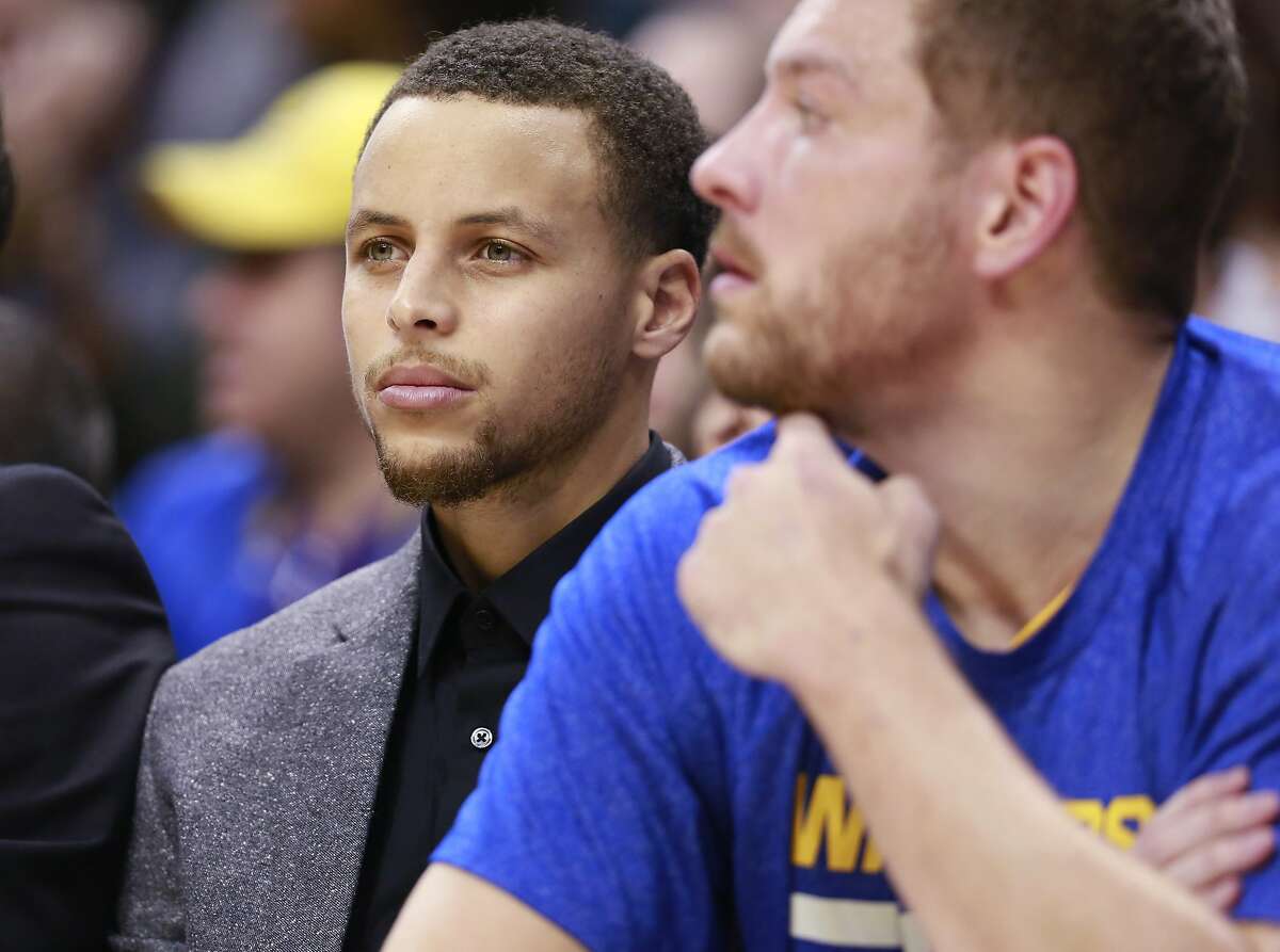 Golden State Warriors guard Stephen Curry, left, sits next to Warriors forward David Lee on the team bench in the first half of an NBA basketball game against the Indiana Pacers, Sunday, Feb. 22, 2015, in Indianapolis. (AP Photo/R Brent Smith)