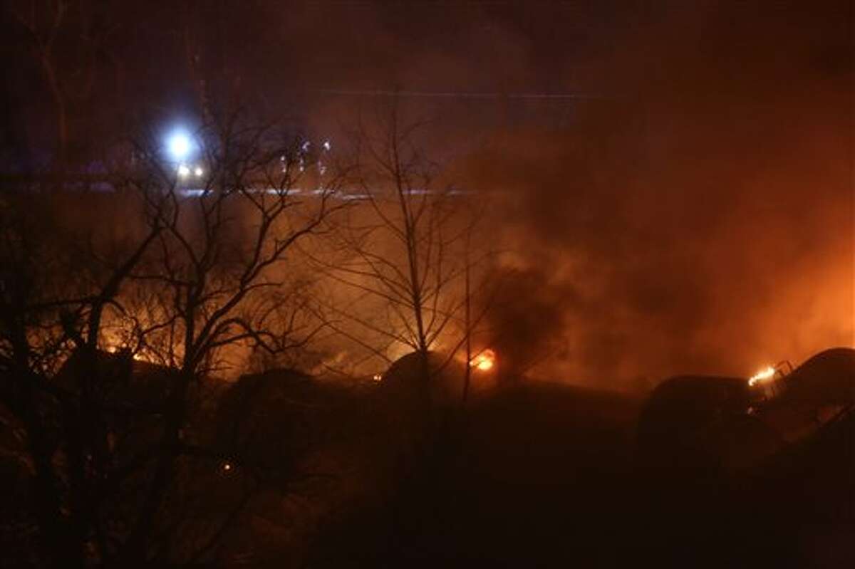 Firefighters look at burning train cars from W.Va. Route 61 near Mount Carbon, W.Va., Monday, Feb. 16, 2015. A CSX train carrying more than 100 tankers of crude oil derailed in a snowstorm, sending a fireball into the sky and threatening the water supply of nearby residents, authorities and residents said Tuesday. (AP Photo/The Daily Mail, Marcus Constantino)