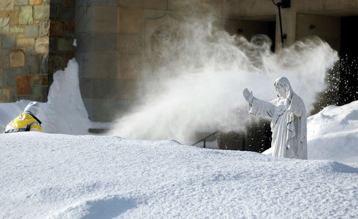 In this Monday, Feb. 16, 2015 photo, custodian George Blomquist clears snow from the grounds of Our Lady of the Angels Church after a weekend snowstorm in Worcester, Mass. Churches, synagogues and mosques in New England report that attendance is down at worship services this winter, as many storms have hit over weekends. (AP Photo/Worcester Telegram & Gazette, Christine Peterson)