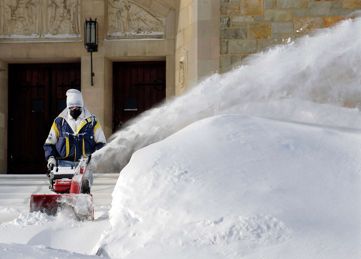 In this Monday, Feb. 16, 2015 photo, custodian George Blomquist clears snow from the sidewalk in front of Our Lady of the Angels Church after a weekend snowstorm in Worcester, Mass. Churches, synagogues and mosques in New England report that attendance is down at worship services this winter, as many storms have hit over weekends. (AP Photo/Worcester Telegram & Gazette, Christine Peterson)