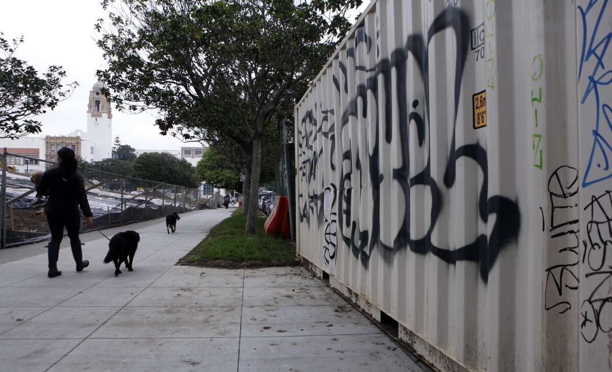 A woman and her dogs walk by a graffitied storage container near the site of new construction at Dolores Park in the Mission District of San Francisco, Calif. Friday, February 20, 2015 after vandals caused $100,00 in damage over the weekend, setting back the date for re-opening indefinitely.