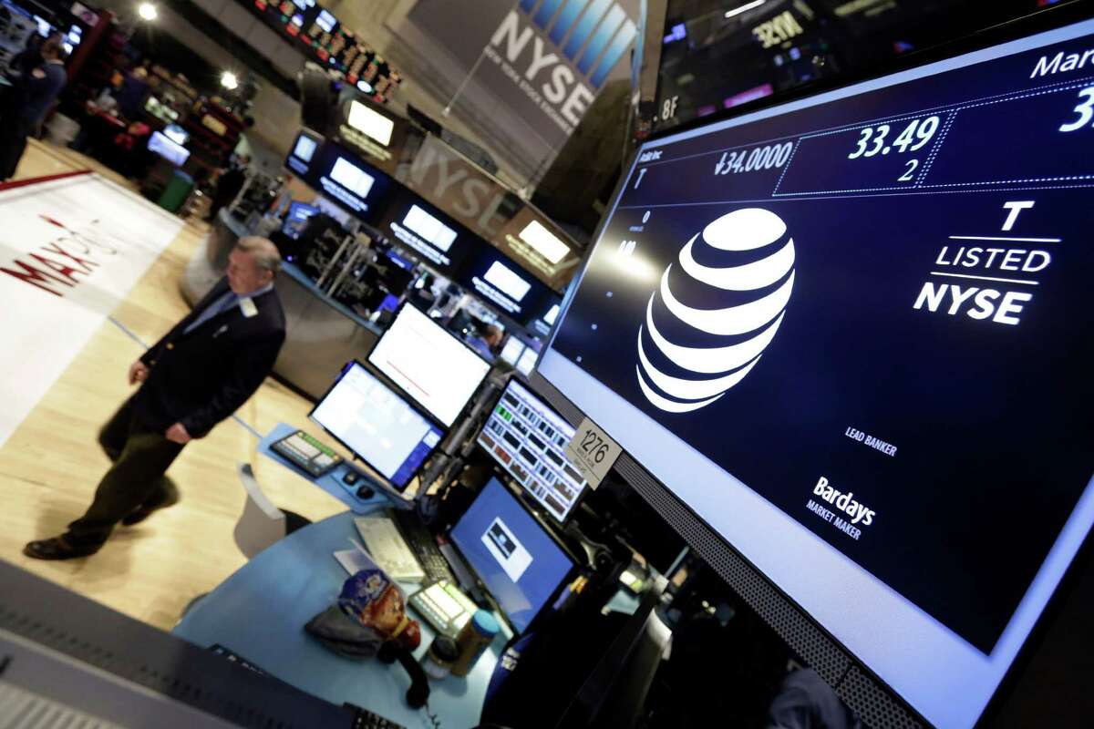 A trader walks by the post that handles AT&T on the floor of the New York Stock Exchange, Friday, March 6, 2015. Apple will replace AT&T in the Dow Jones industrial average, the managers of the index announced early Friday. (AP Photo/Richard Drew)