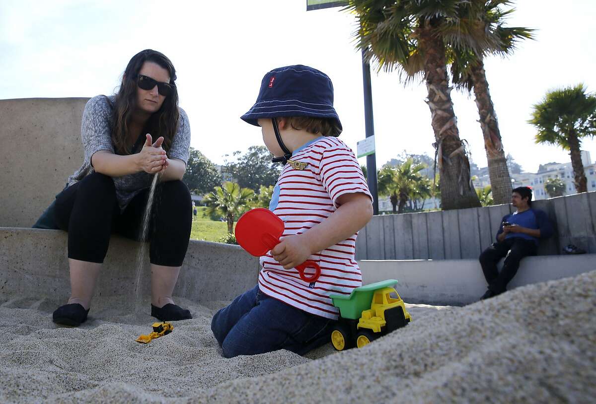 Nanny Carly Studzinski feels the sand as Sebastian Berle-Smith, 2 years old, plays at the sandbox filled with new sand in the children's playground at Dolores Park in San Francisco, California on Monday, March 9, 2015. Twenty tons of sand replaced polluted sand by vandals breaking bottles a few weeks ago