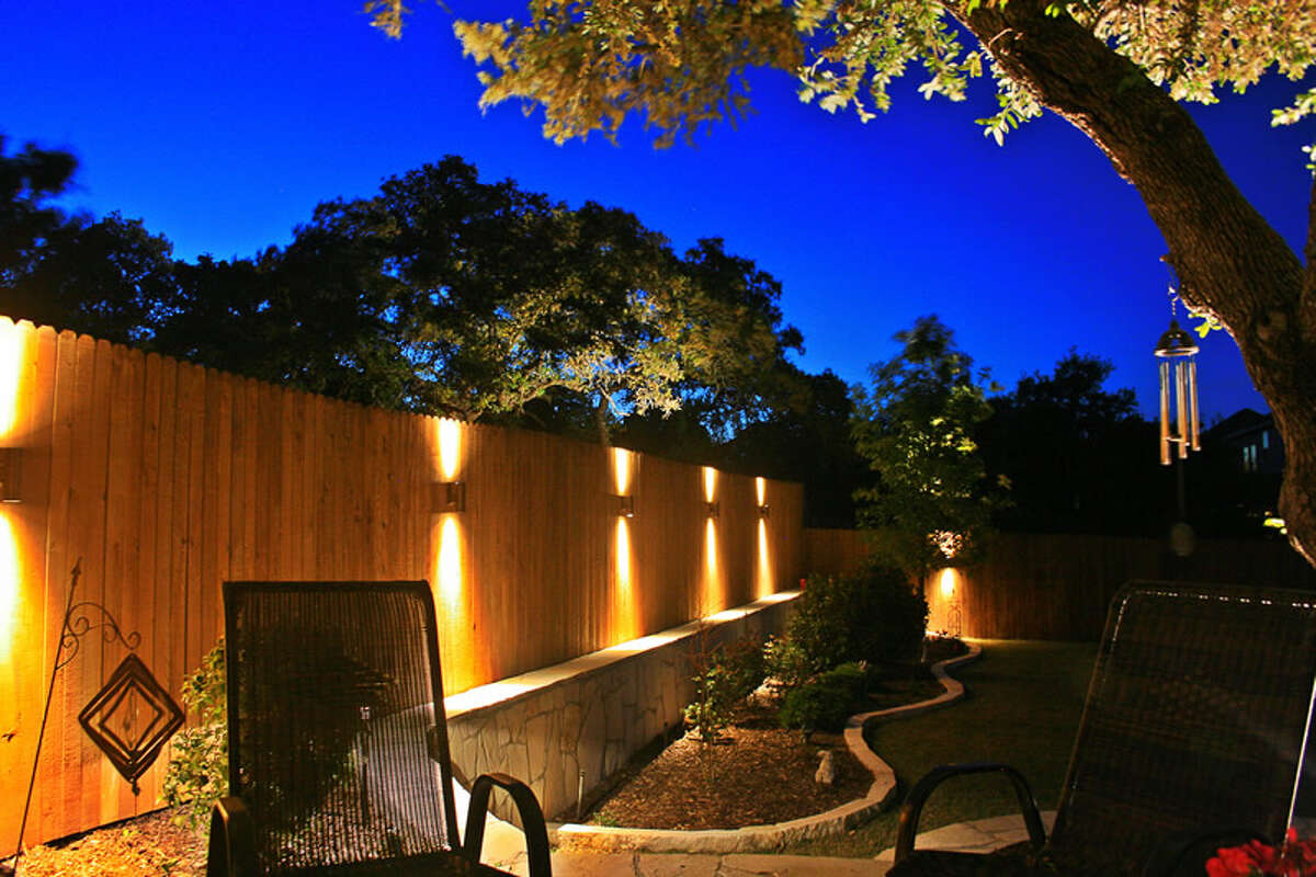 Illuminated sconces add interest and draw the eye to a fence in a design by Bolt Outdoor Lighting.