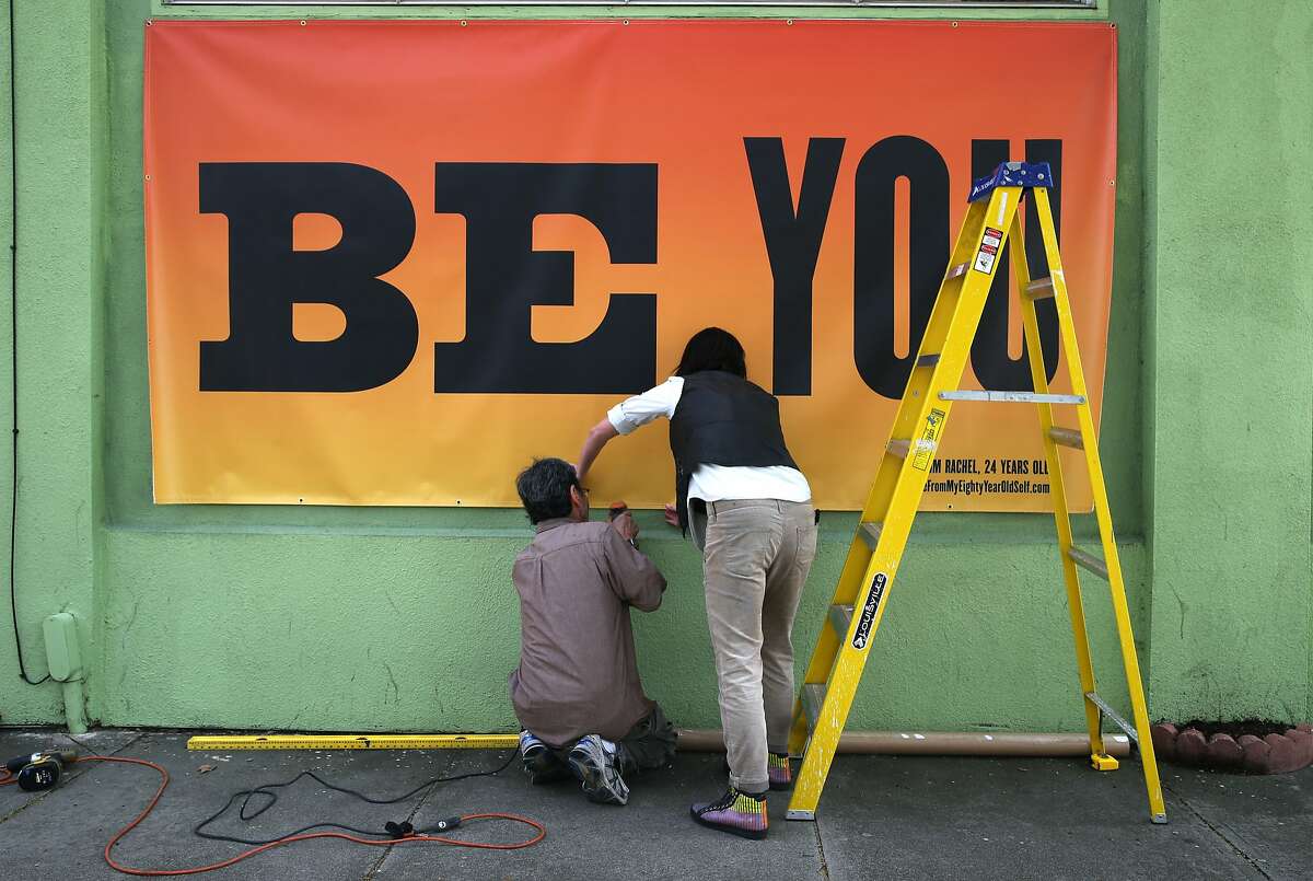 Kala Art exhibit curator Amanda Curreri (right) installs an art project created by artist Susan O'Malley on a San Pablo Avenue business in Berkeley, Calif. on Wednesday, March 11, 2015. O'Malley died tragically a week before she was due to deliver twin girls. Her art project, "Advice From My 80-year-old Self" is part of an exhibition at the Kala Art Institute in Berkeley opening May 7.