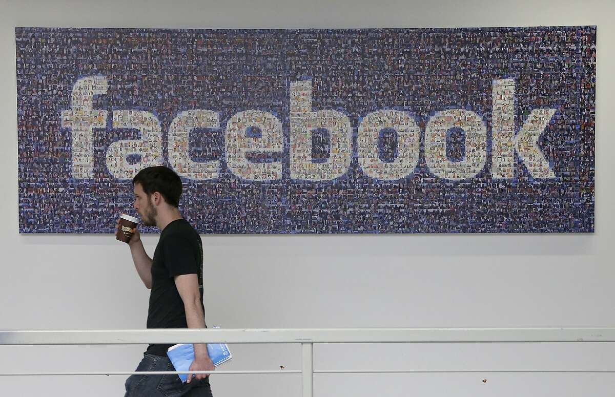 In this March 15, 2013, file photo, a Facebook employee walks past a sign at Facebook headquarters in Menlo Park, Calif. Facebook is giving more options to decide what happens to users' accounts after they die. The world's biggest online social network will now let users pick a trusted contact who can manage their account or elect to have the account deleted, the company announced, Thursday, Feb. 12, 2015. (AP Photo/Jeff Chiu, File)