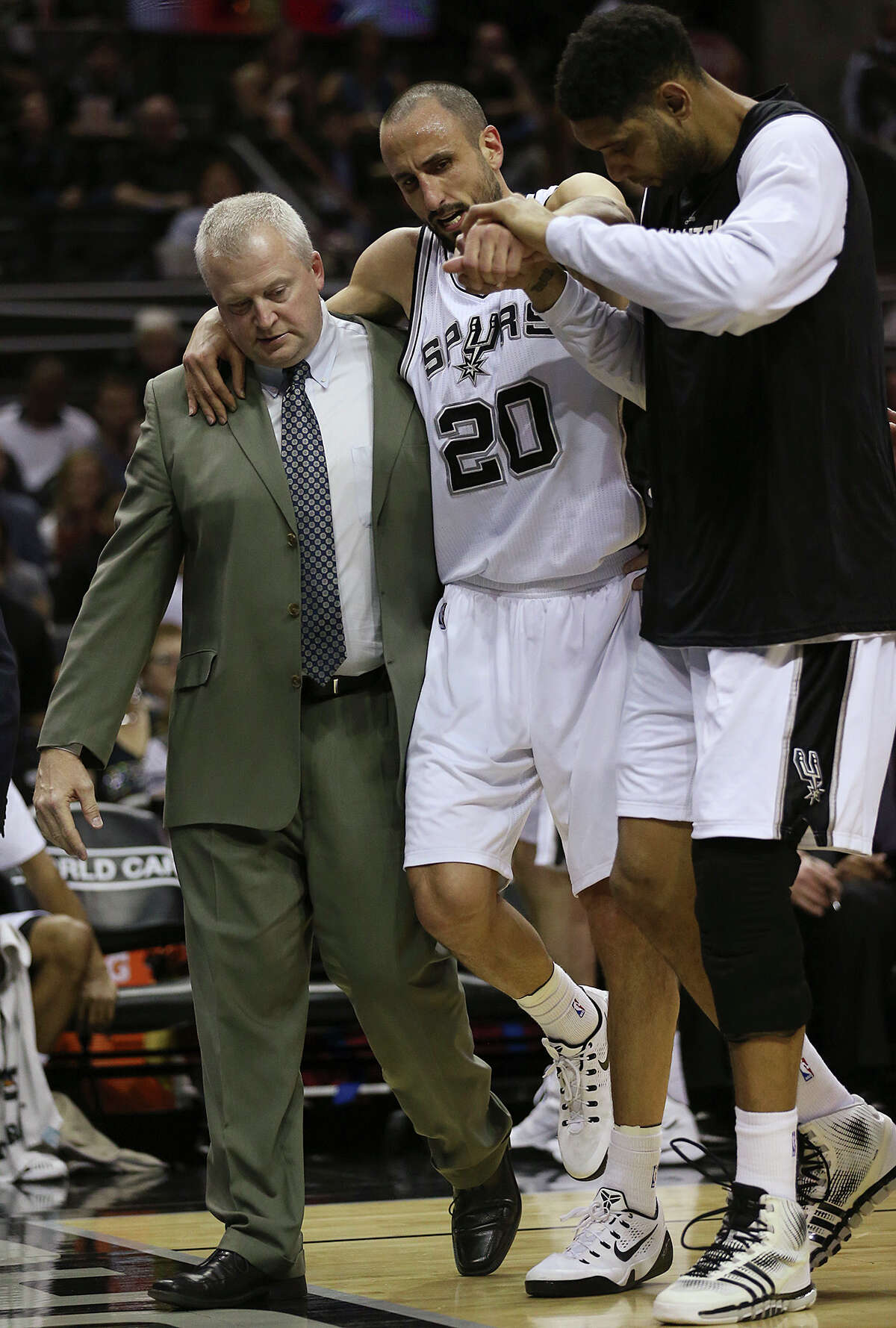 The Spurs’ Manu Ginobili is helped off the court by head athletic trainer Will Sevening and Tim Duncan during the second half at the AT&T Center on March 15, 2015.