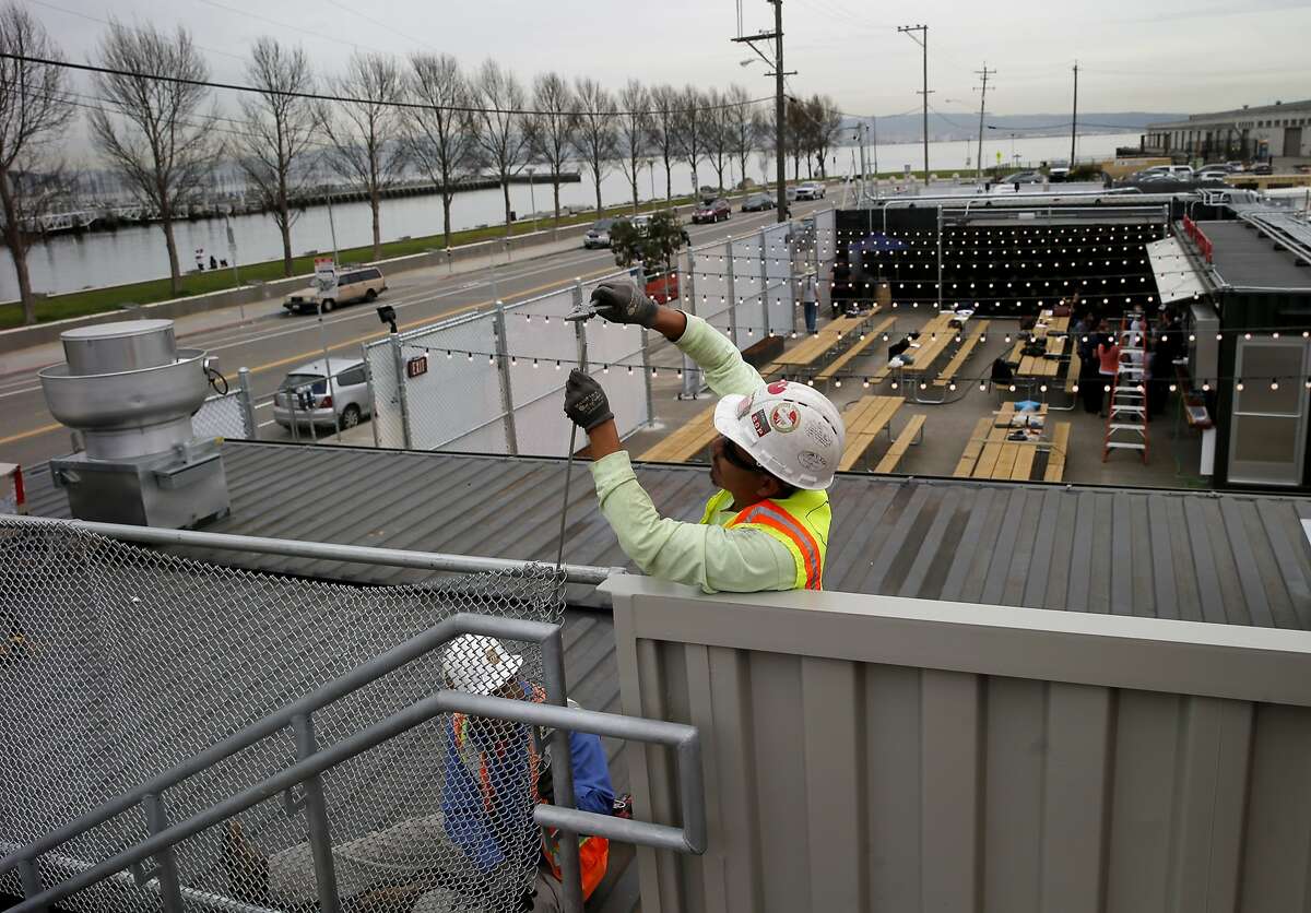 Workers complete a cyclone fence to keep visitors off the roof of one container Monday March 16, 2015. The Giants' Yard at Mission Rock bills itself as a pop-up shipping container village that has local food and drink, public space and events. It joins other shipping container stores like Proxy at Octavia and Hayes Streets in San Francisco, Calif.