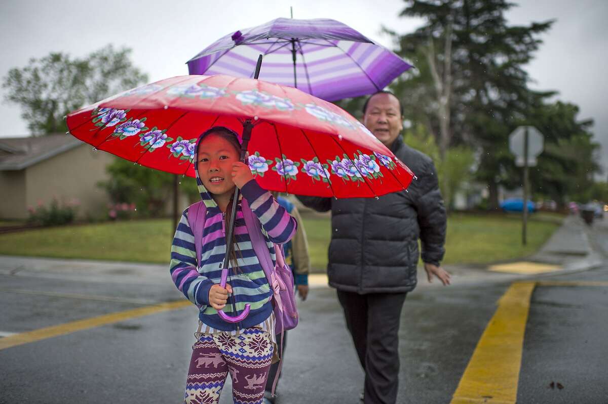 Cecilia Xiong, left, and her father, Kachang Xiong, walk to Parkway Elementary School, Tuesday, April 7, 2015, in Sacramento, Calif. An unusually cold spring storm brought heavy rain and hail to parts of Northern California on Tuesday and coated the mountains in snow.