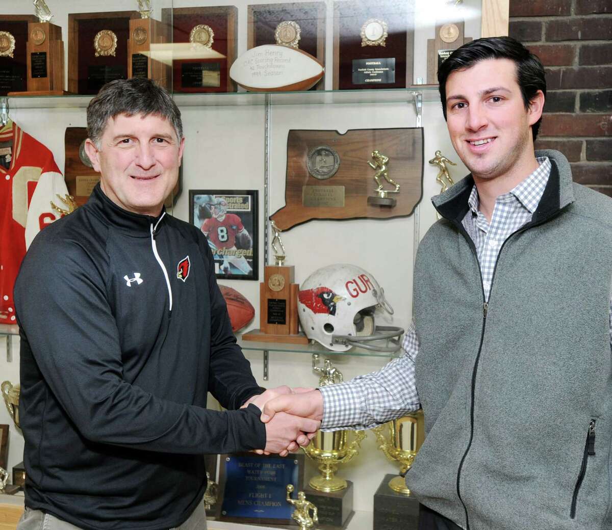 At left, Gus Lindine, Greenwich High School athletic director, shakes hands with John Marinelli who was named the new Greenwich High School football coach during an announcement at the school in Greenwich, Conn., Wednesday, April 8, 2015. Marinelli is the son of New Canaan High School football coach, Lou Marinelli. John Marinelli served as an assistant football coach at New Canaan High School under his father.