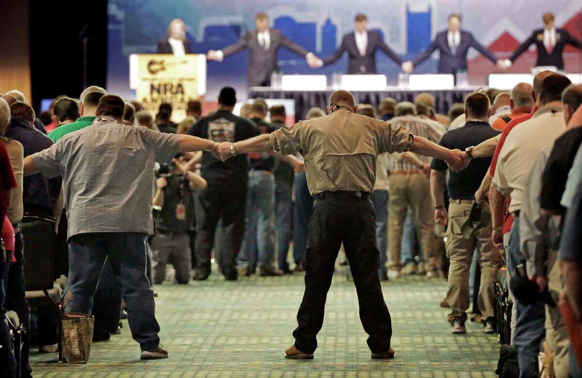 National Rifle Association members hold hands during the opening prayer at the annual meeting of members at the NRA convention on Saturday. The group is concerned about potential efforts to limit the right to own guns.