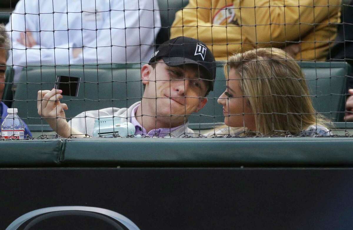 Cleveland Browns quarterback Johnny Manziel, left, sits in the stands during a baseball game between the Los Angeles Angels and Texas Rangers in Arlington, Texas, Tuesday, April 14, 2015. (AP Photo/LM Otero)