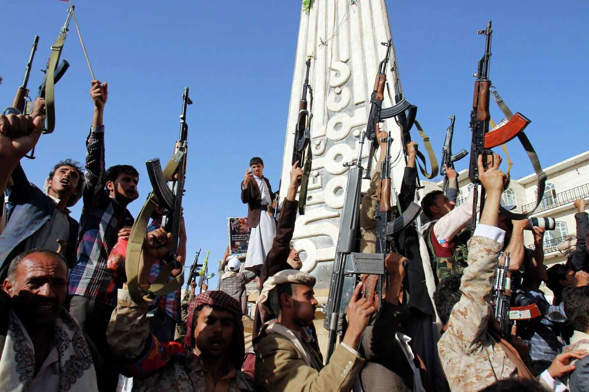 A man (background) uses his cellphone to take a photo of Shiite rebels, known as Houthis, holding up their weapons in Sanaa, Yemen, during a demonstration against a U.N. Security Council-imposed arms embargo on Houthi leaders.