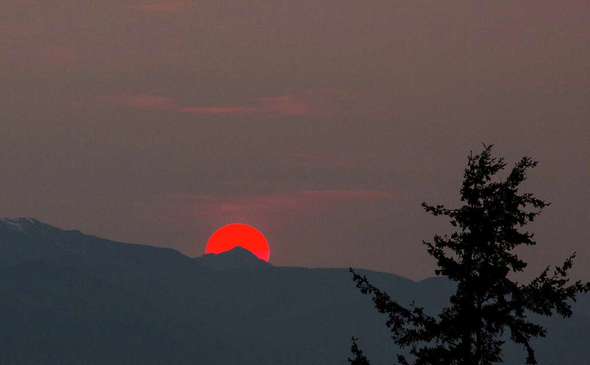 A sun tinted red by grass fires in Siberia sets behind the Olympic Mountains on Saturday, April 18, 2015.