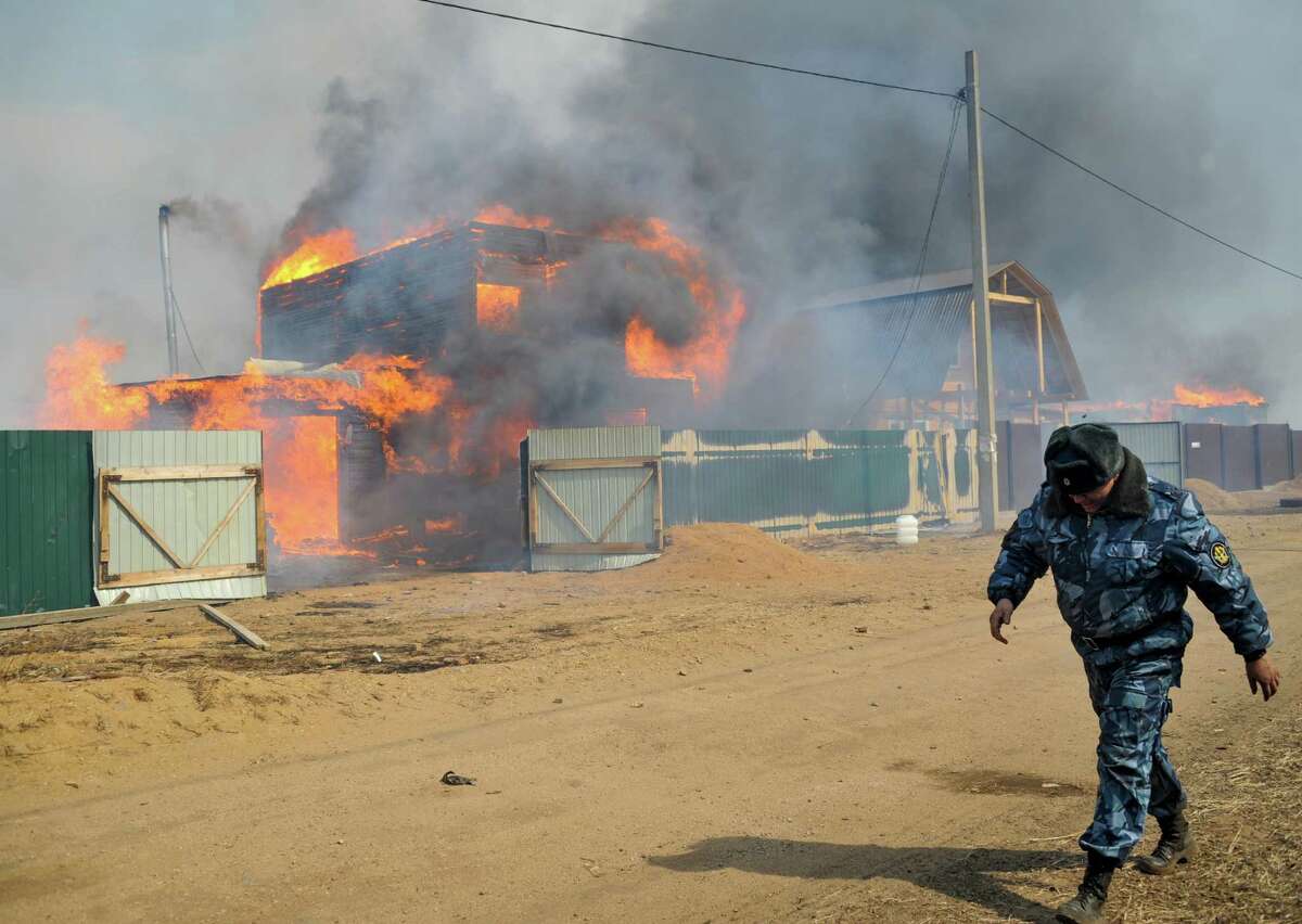 A police officer walks along a street of the burning village of Smolenka near Chita on Monday, April 13, 2015. Russian authorities say out-of-control agricultural fires have killed at least 15 people, injured hundreds more and destroyed or damaged more than 1,000 homes in Siberia. The fires were started by farmers burning the grass in their fields, but spread quickly because of strong winds.
